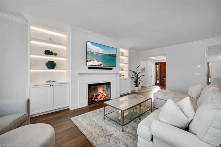 Living room featuring built in features, ornamental molding, a glass covered fireplace, and dark wood-style floors