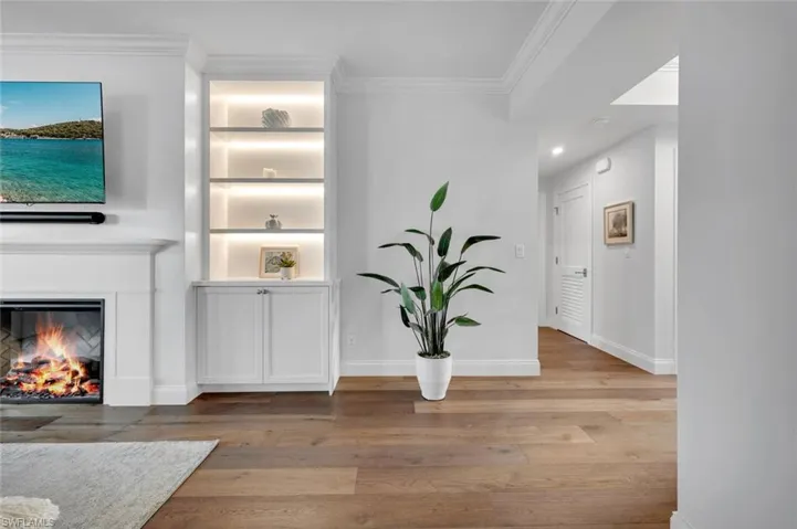 Living area with ornamental molding, light wood-style floors, and a glass covered fireplace