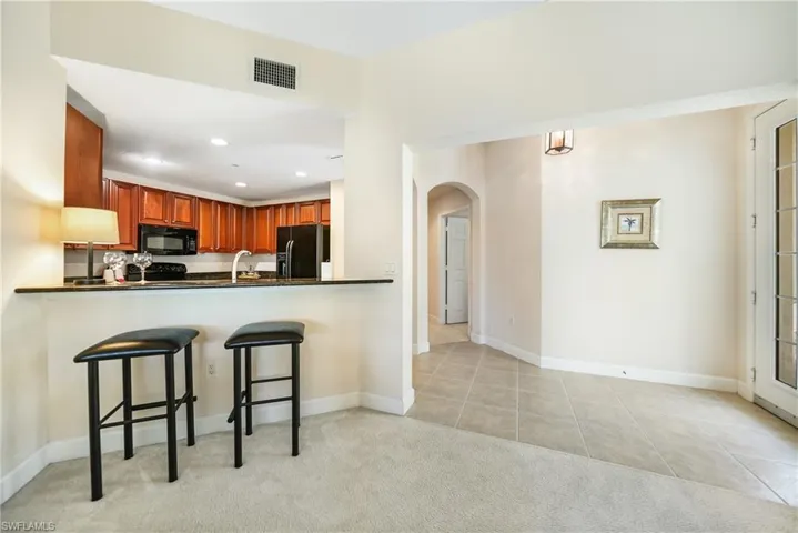 Kitchen featuring sink, a breakfast bar area, kitchen peninsula, light colored carpet, and black appliances