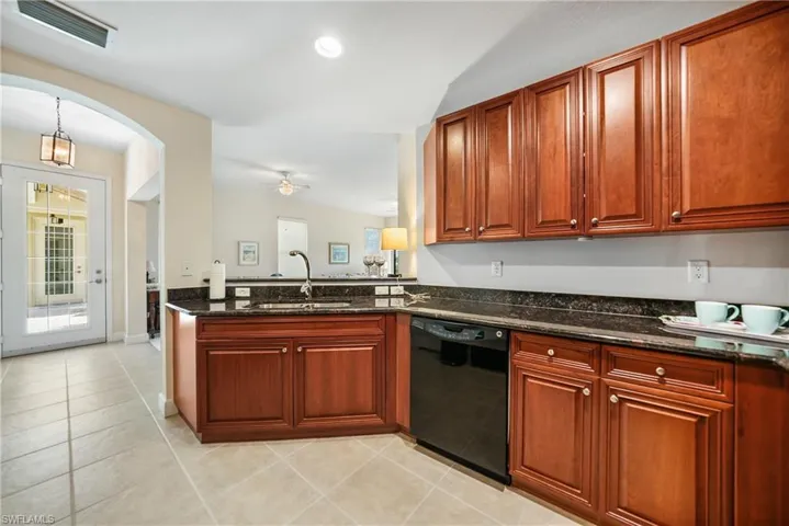 Kitchen featuring black dishwasher, light tile patterned flooring, sink, and dark stone counters