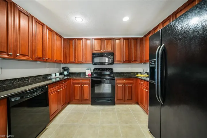 Kitchen featuring dark stone countertops, black appliances, and light tile patterned floors