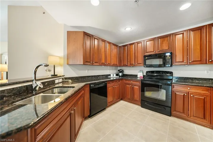 Kitchen with sink, dark stone counters, black appliances, and light tile patterned flooring