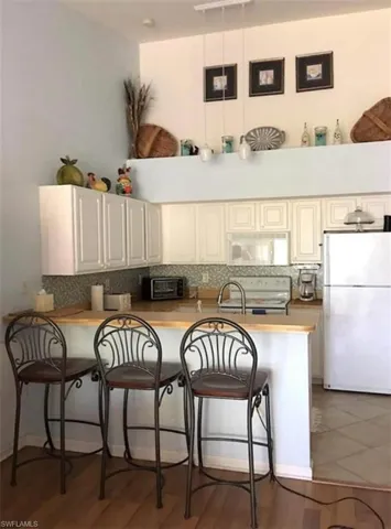 Kitchen with a breakfast bar area, kitchen peninsula, backsplash, and white appliances
