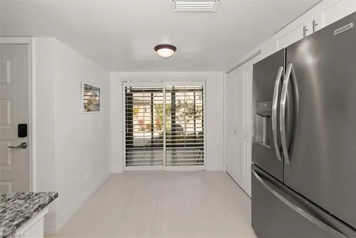Kitchen with stainless steel fridge, white cabinets, and light stone countertops