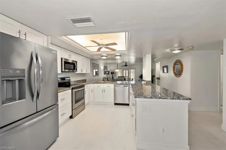 Kitchen featuring appliances with stainless steel finishes, a peninsula, a tray ceiling, white cabinetry, and dark stone counters