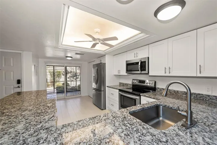 Kitchen featuring stainless steel appliances, dark stone countertops, a tray ceiling, and ceiling fan