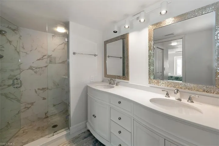 Full bath featuring a marble finish shower and double vanity