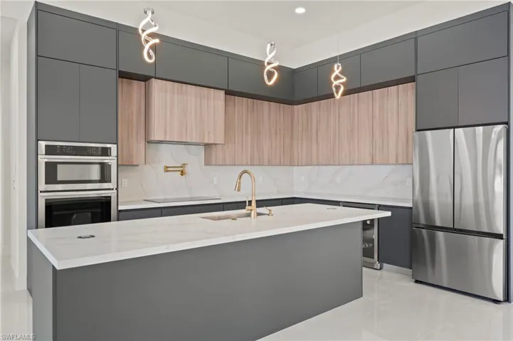 Kitchen featuring stainless steel appliances, a sink, backsplash, modern cabinets, and a center island with sink