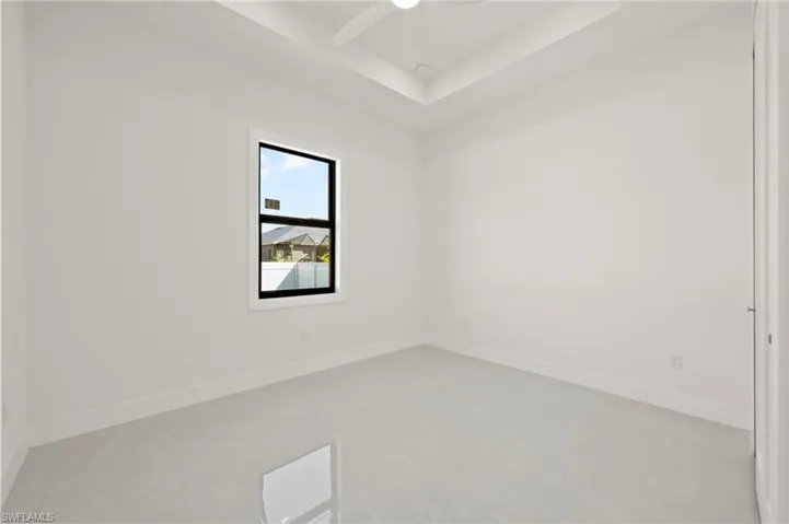 Empty room with concrete flooring, a tray ceiling, baseboards, and a ceiling fan