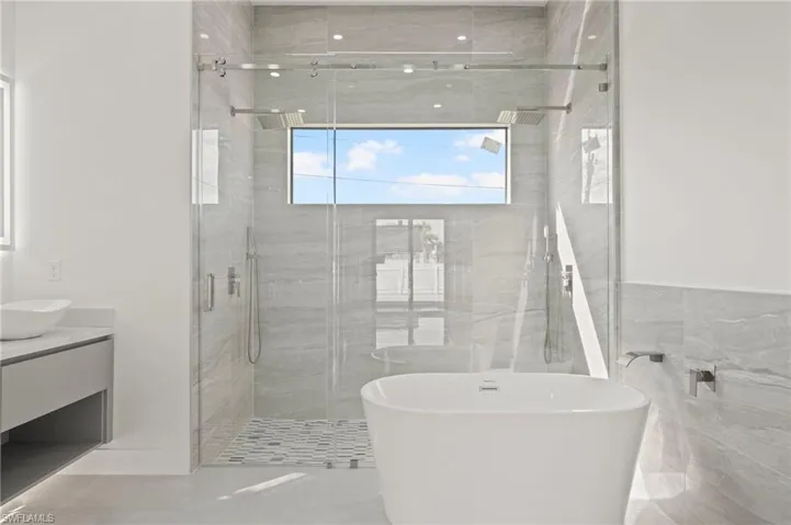 Full bath featuring a freestanding bath, a shower stall, vanity, and tile walls