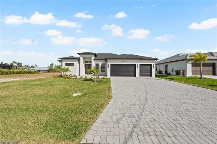 Prairie-style home with a front yard, decorative driveway, an attached garage, and stucco siding