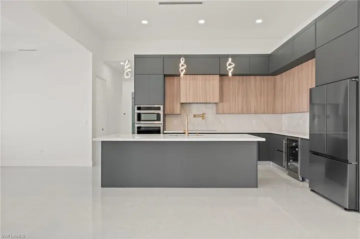 Kitchen with tasteful backsplash, wine cooler, modern cabinets, appliances with stainless steel finishes, and light countertops