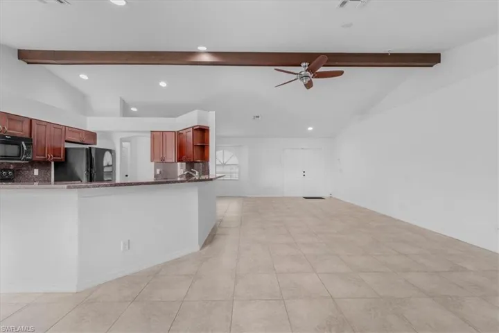 Kitchen featuring vaulted ceiling, dark stone countertops, a ceiling fan, tasteful backsplash, and black appliances