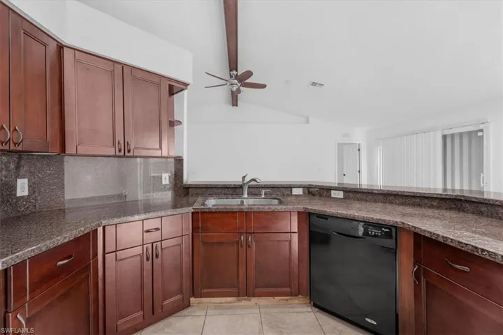 Kitchen featuring black dishwasher, dark stone countertops, open shelves, decorative backsplash, and vaulted ceiling with beams