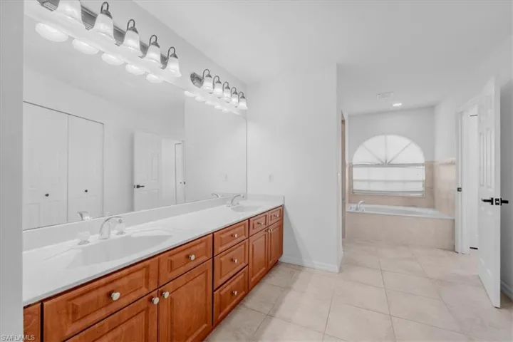 Full bathroom with a garden tub, double vanity, light tile patterned floors, and a closet