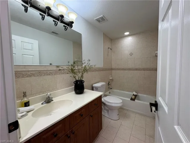 Bathroom with vanity, tile walls, shower / tub combination, light tile patterned floors, and a textured ceiling