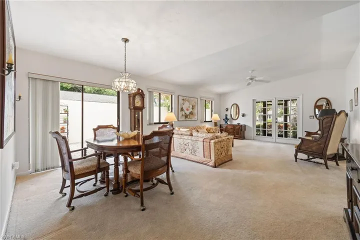 Dining room with lofted ceiling, light carpet, healthy amount of natural light, a chandelier, and a ceiling fan