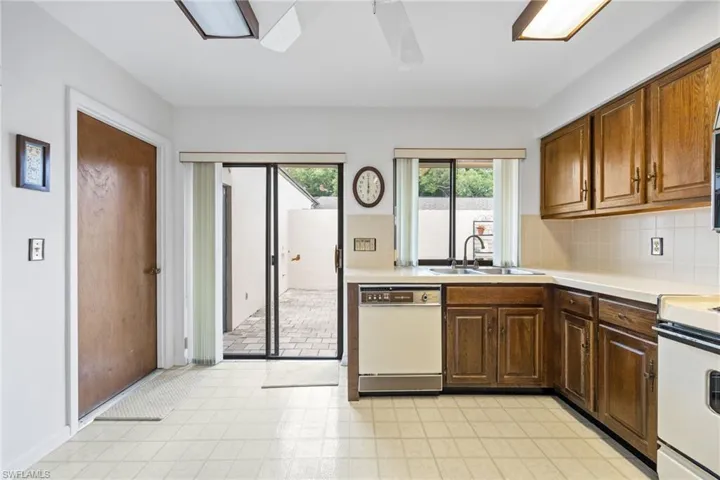Kitchen with white appliances, decorative backsplash, light flooring, dark brown cabinets, and ceiling fan