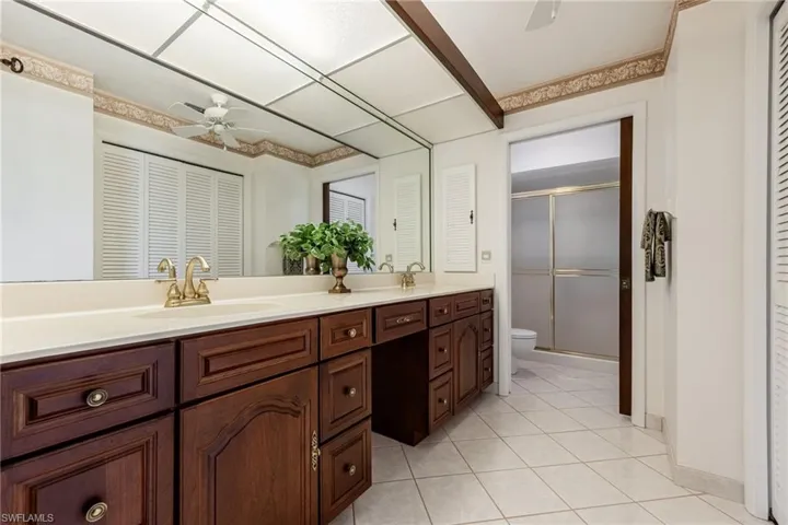 Bathroom featuring a closet, ceiling fan, double vanity, a shower stall, and light tile patterned floors