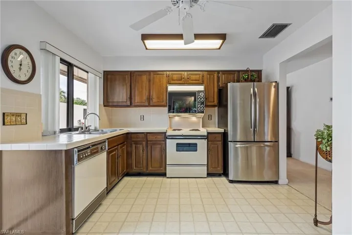 Kitchen with white appliances, light flooring, backsplash, and a ceiling fan