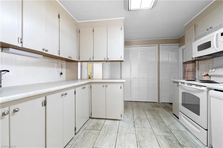 Kitchen featuring white appliances, light countertops, decorative backsplash, and white cabinets