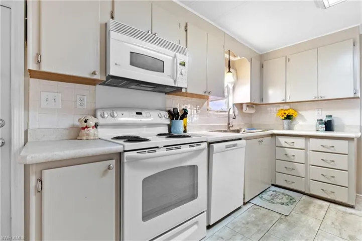 Kitchen featuring light countertops, white appliances, a sink, backsplash, and light tile patterned floors