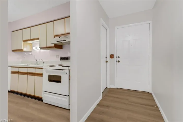 Kitchen with sink, white electric stove, light hardwood / wood-style flooring, and cream cabinetry