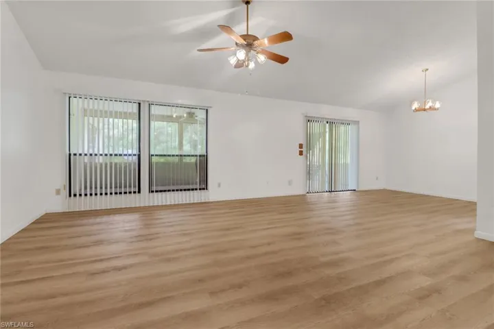 Main living room featuring plenty of natural light, ceiling fan with notable chandelier, light hardwood / wood-style flooring, and lofted ceiling