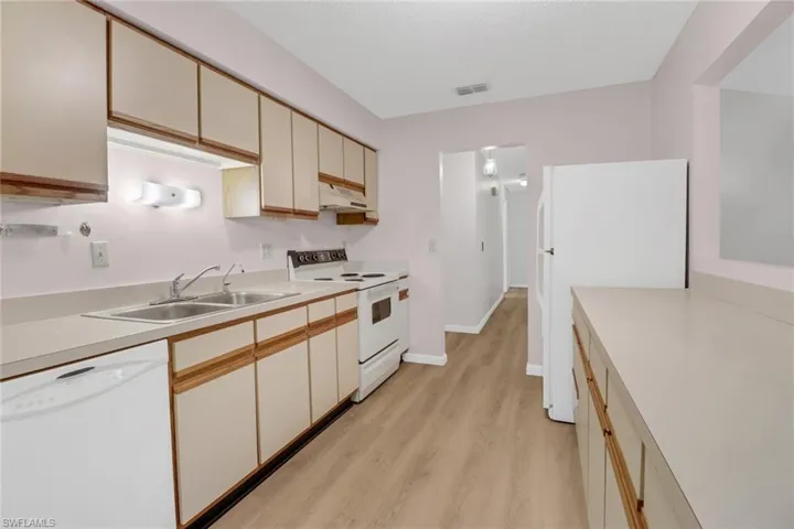 Kitchen with cream cabinets, sink, white appliances, and light hardwood / wood-style floors