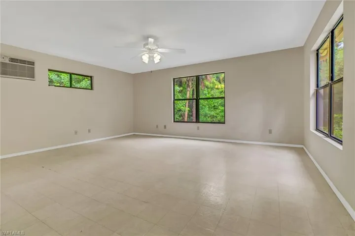 Tiled spare room featuring a wall mounted air conditioner, ceiling fan, and plenty of natural light