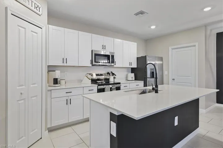 Kitchen with appliances with stainless steel finishes, an island with sink, white cabinetry, light stone countertops, and recessed lighting