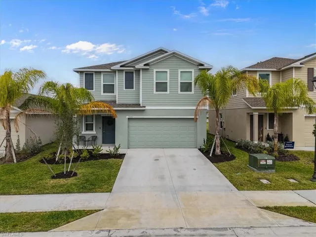 Traditional-style home with a front yard, driveway, a garage, stucco siding, and roof with shingles