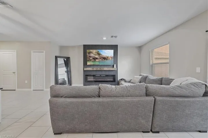Living area with light tile patterned flooring, a glass covered fireplace, and recessed lighting
