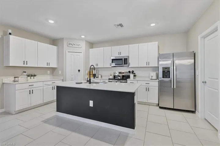 Kitchen with appliances with stainless steel finishes, white cabinets, an island with sink, recessed lighting, and light tile patterned floors