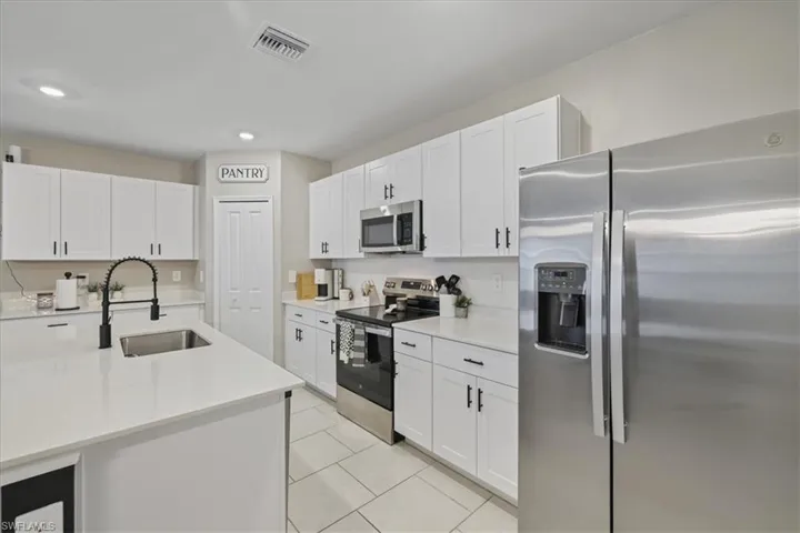 Kitchen with appliances with stainless steel finishes, white cabinetry, light stone countertops, light tile patterned flooring, and recessed lighting