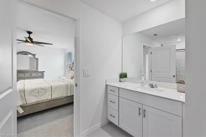 Bathroom featuring vanity, curtained shower, light colored carpet, ceiling fan, and ensuite bathroom