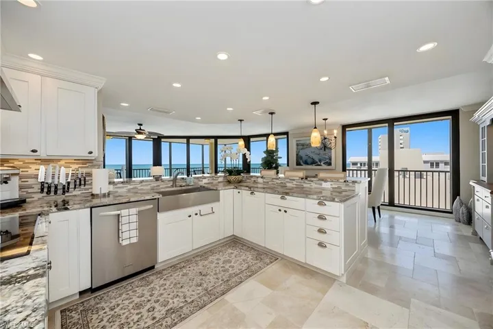 Kitchen with white cabinets, a peninsula, light stone countertops, stainless steel dishwasher, and decorative light fixtures