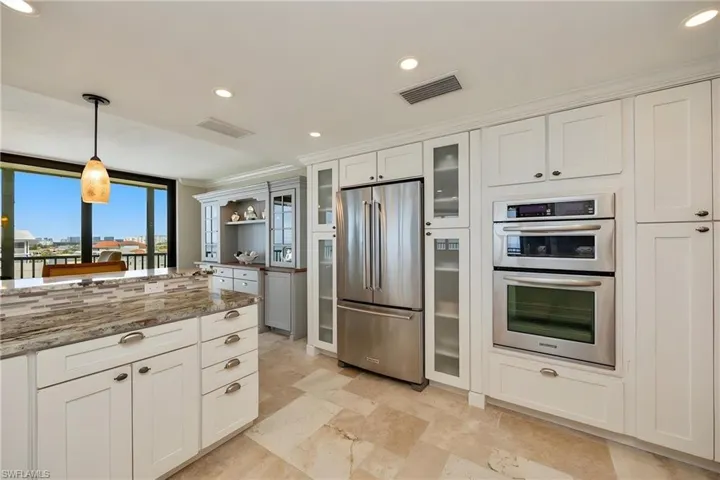 Kitchen with white cabinetry, pendant lighting, stainless steel appliances, glass fronted cabinets, and dark stone countertops