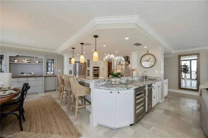 Kitchen with white cabinets, light stone countertops, a kitchen breakfast bar, ornamental molding, and decorative light fixtures