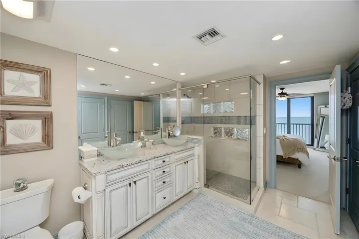Ensuite bathroom with double vanity, a shower stall, a water view, recessed lighting, and ceiling fan