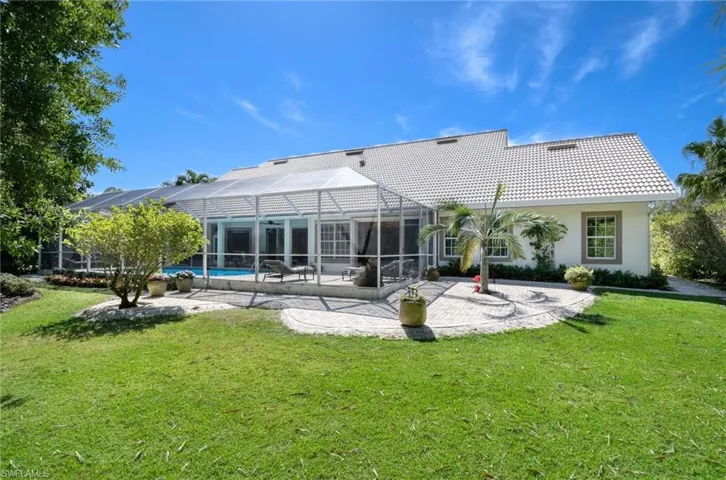 Back of the home which offers a tiled roof, lovely lawn area, and patio.