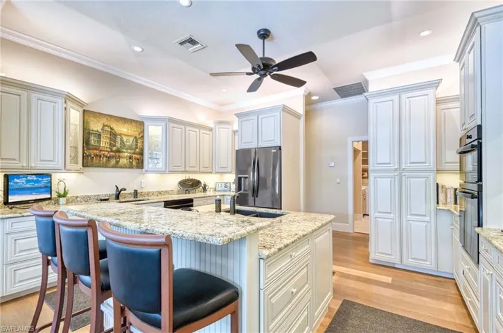 Kitchen featuring crown molding, Center Island with vegetable sink, and black cooktop and wall oven.