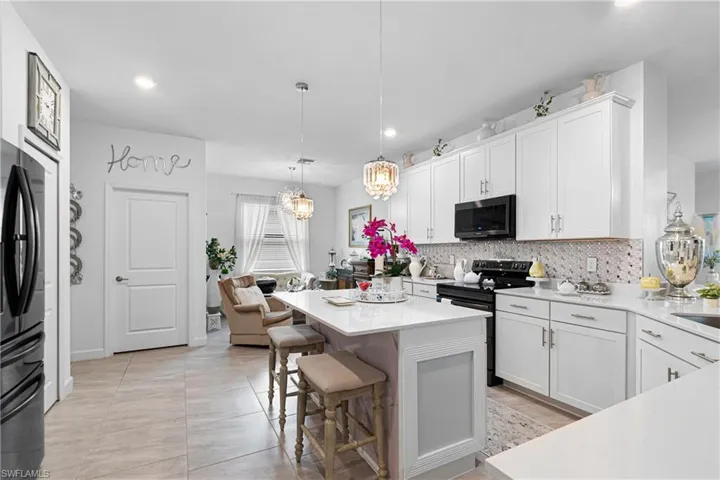 Kitchen with range with electric stovetop, backsplash, light countertops, white cabinets, and black refrigerator