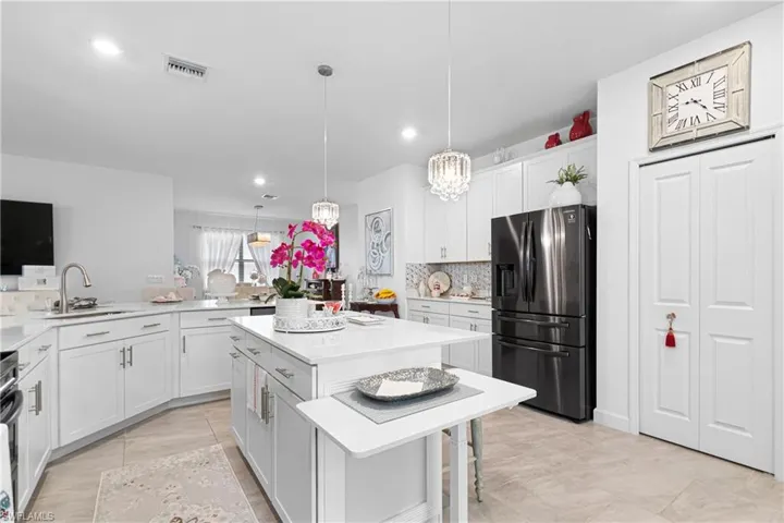 Kitchen with stainless steel fridge, backsplash, light countertops, white cabinets, and recessed lighting