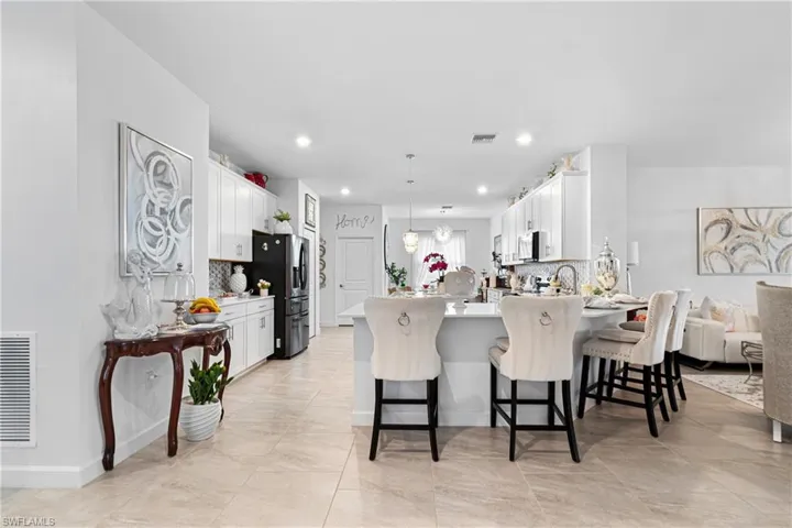 Kitchen with a peninsula, white cabinets, a kitchen bar, decorative backsplash, and recessed lighting