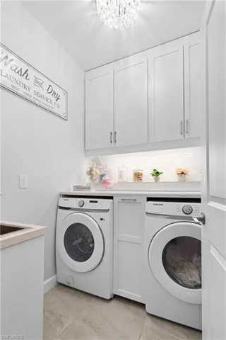 Laundry area featuring cabinet space, washing machine and clothes dryer, light tile patterned floors, and a chandelier