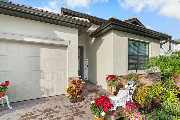Entrance to property with stone siding, an attached garage, stucco siding, and a tiled roof