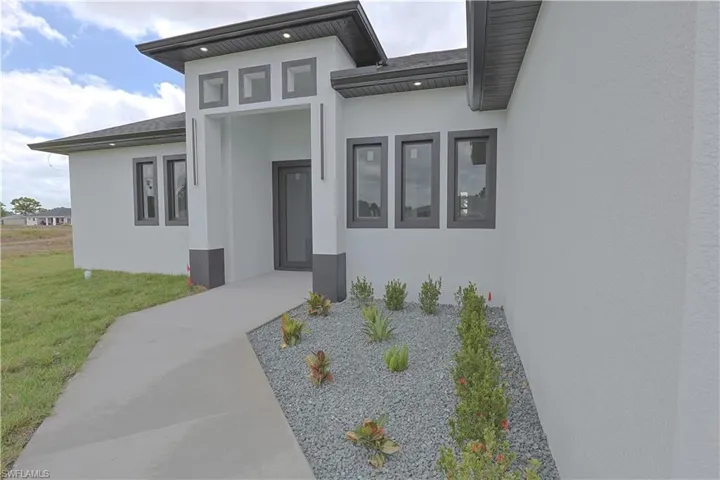 Property entrance featuring stucco siding, a shingled roof, and a lawn