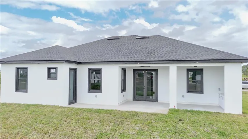Rear view of house featuring stucco siding, a shingled roof, french doors, and a yard