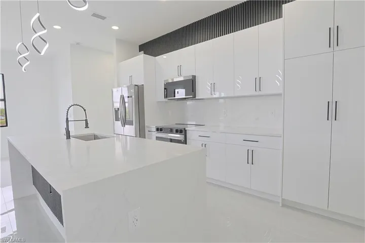 Kitchen with a sink, stainless steel appliances, a kitchen island with sink, visible vents, and white cabinets